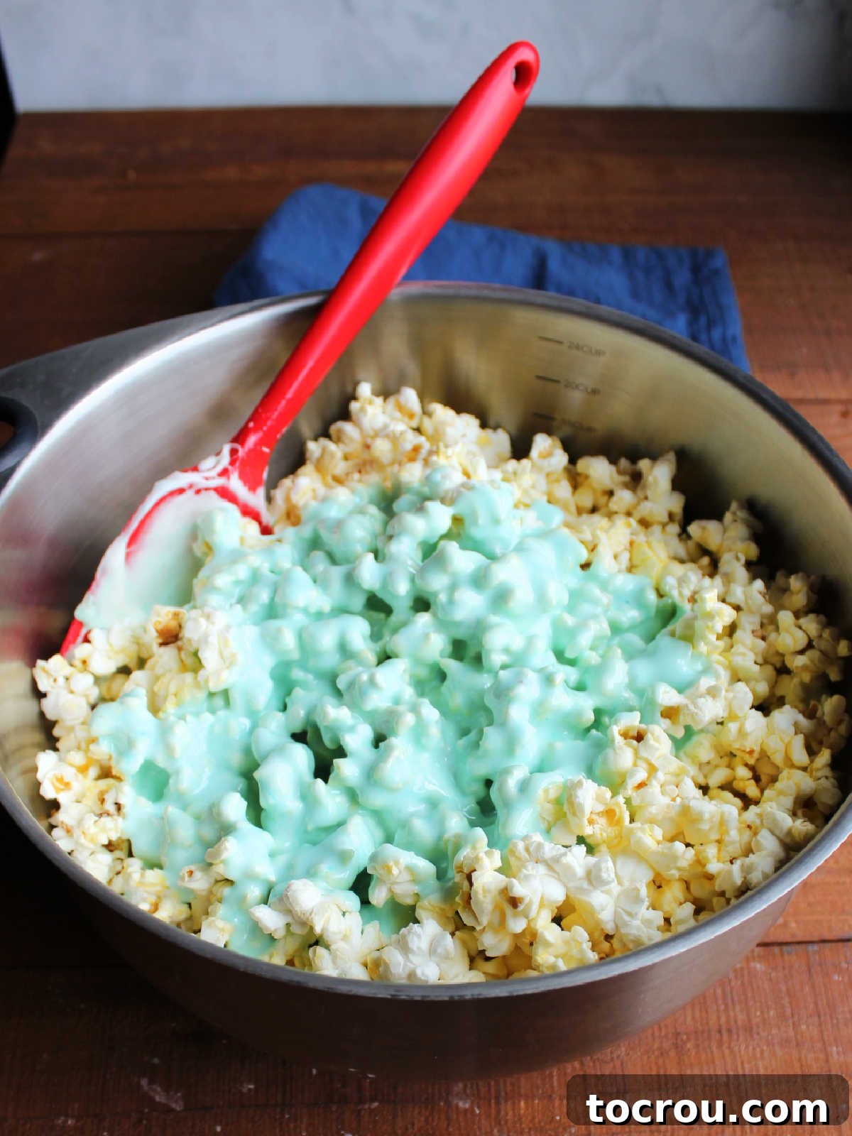 Blue Jell-O marshmallow mixture poured over a large mixing bowl of popcorn, ready to be gently stirred together.