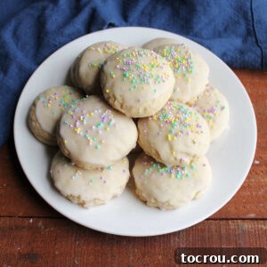 A plate featuring pristine white tea cake cookies, elegantly finished with a delicate powdered sugar glaze and adorned with charming pastel sprinkles.