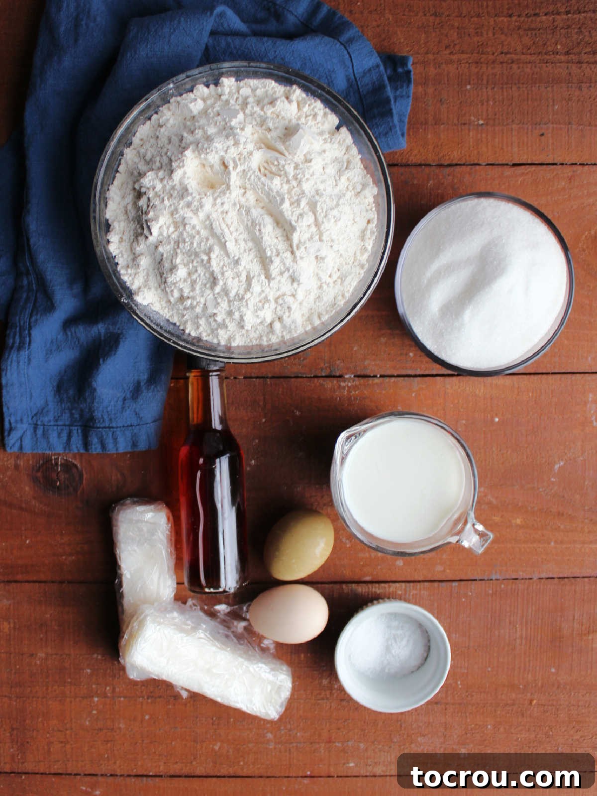 Heirloom Tea Cakes 5 A collection of fresh ingredients neatly arranged, including vibrant green bags of flour, gleaming granulated sugar, creamy soured milk, farm-fresh eggs, a block of lard, a bottle of rich vanilla extract, sparkling salt, and baking soda, all prepared to be transformed into a batch of grandma's cherished white cookies.
