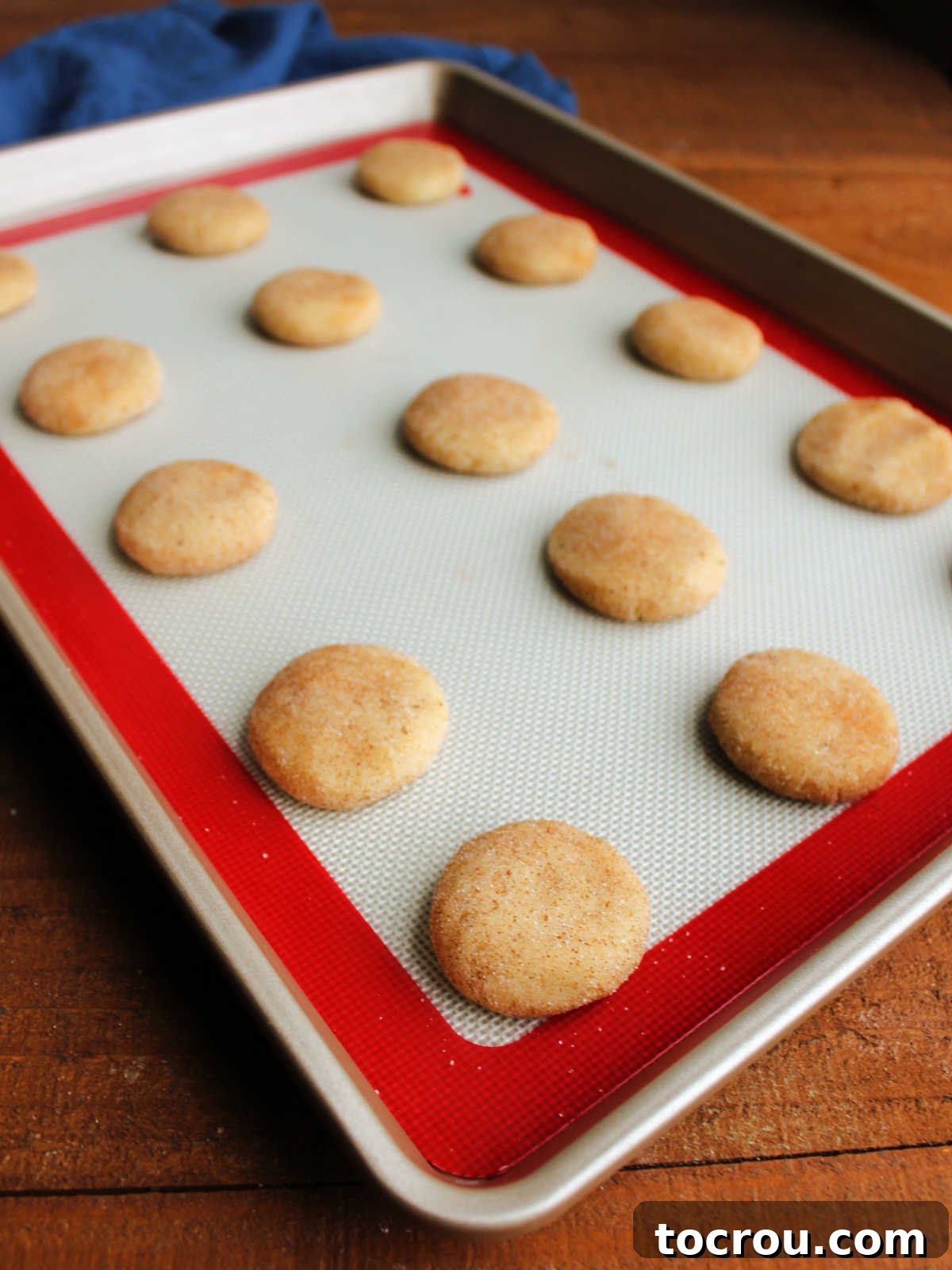 Heirloom Tea Cakes 9 Scoops of delicate dough, each thoroughly coated in a delightful mixture of pumpkin pie spice and sugar, then carefully flattened on a baking sheet lined with a silicone mat, awaiting their transformation in the oven.