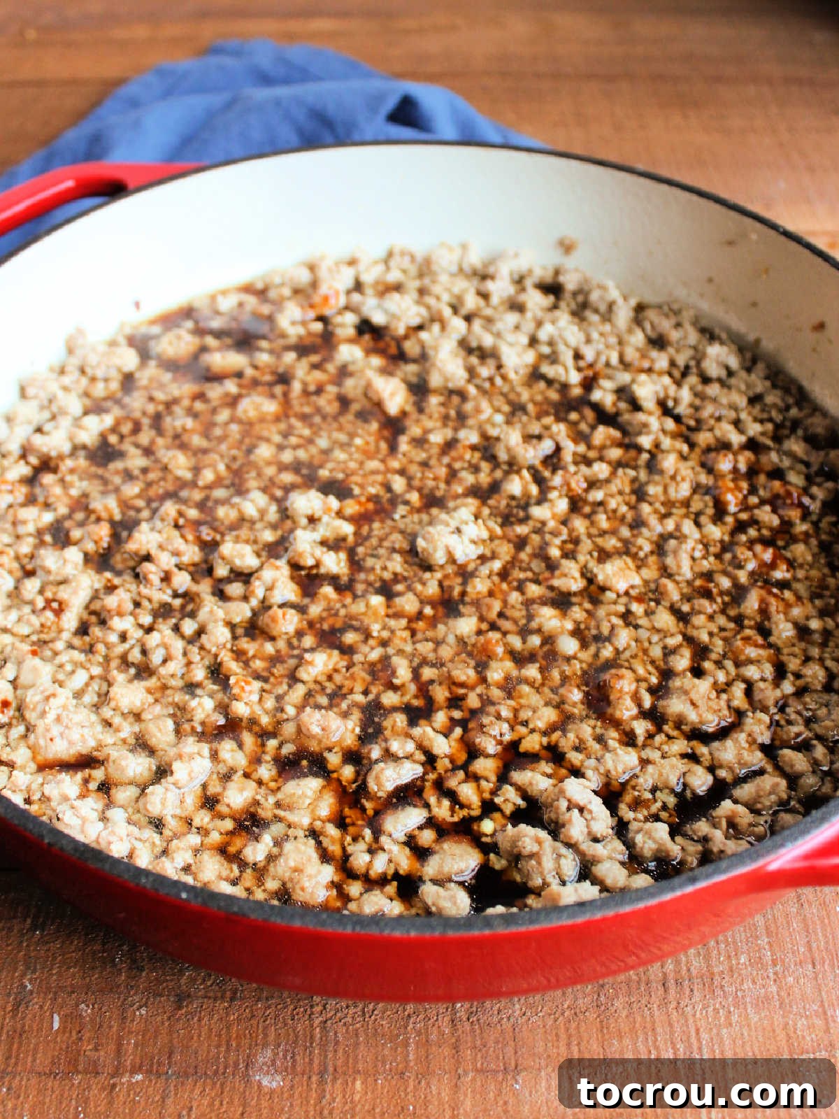 Rich, glossy Asian-inspired sauce simmering in a pan with browned ground pork, featuring soy sauce, hoisin, and other savory ingredients for deep flavor.