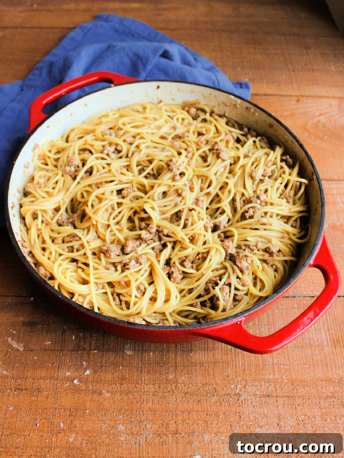 Cooked spaghetti noodles being tossed in a pan with the thick, dark Mongolian sauce and ground pork, ensuring every strand is coated.