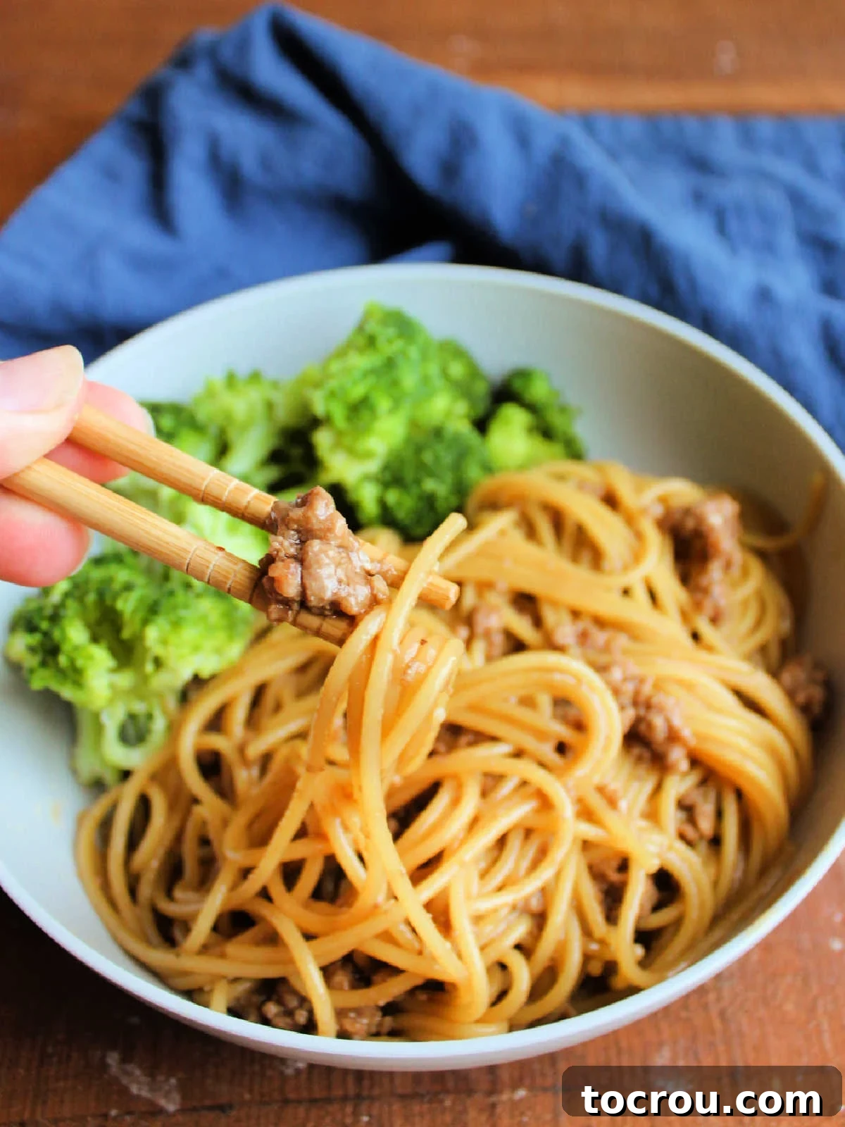 Chopsticks picking up a bite of pasta generously coated with Mongolian ground pork, sesame seeds, and rich Asian-inspired sauce.