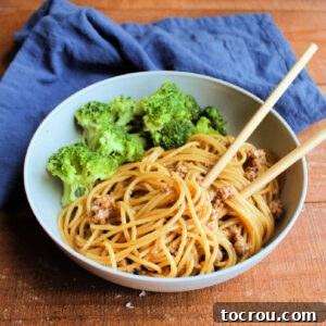 Bowl of ground pork and spaghetti with Asian inspired sauce served with steamed broccoli and bamboo chop sticks, ready to eat.