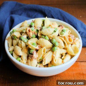 Serving bowl filled with creamy pasta salad with shell shaped noodles, vibrant green peas, and crispy bacon.