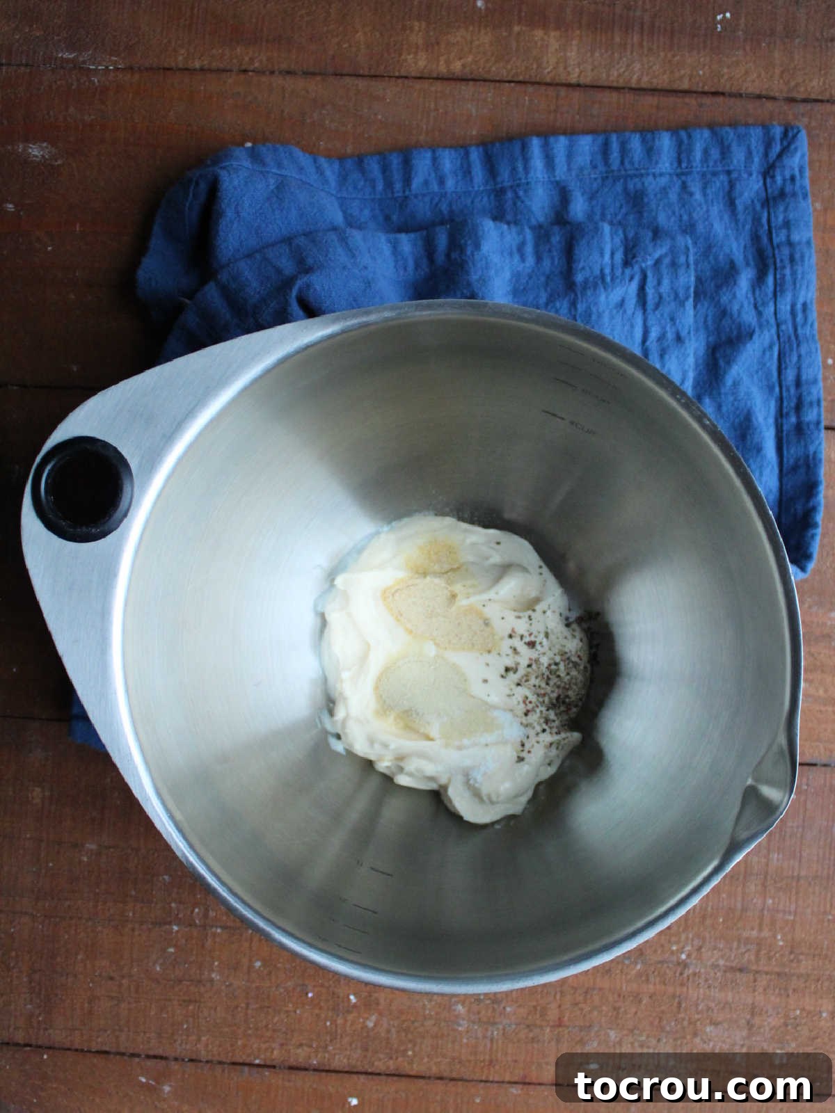 Large mixing bowl with Miracle Whip, garlic powder, onion powder, salt, and pepper inside, demonstrating the preparation of the creamy dressing.