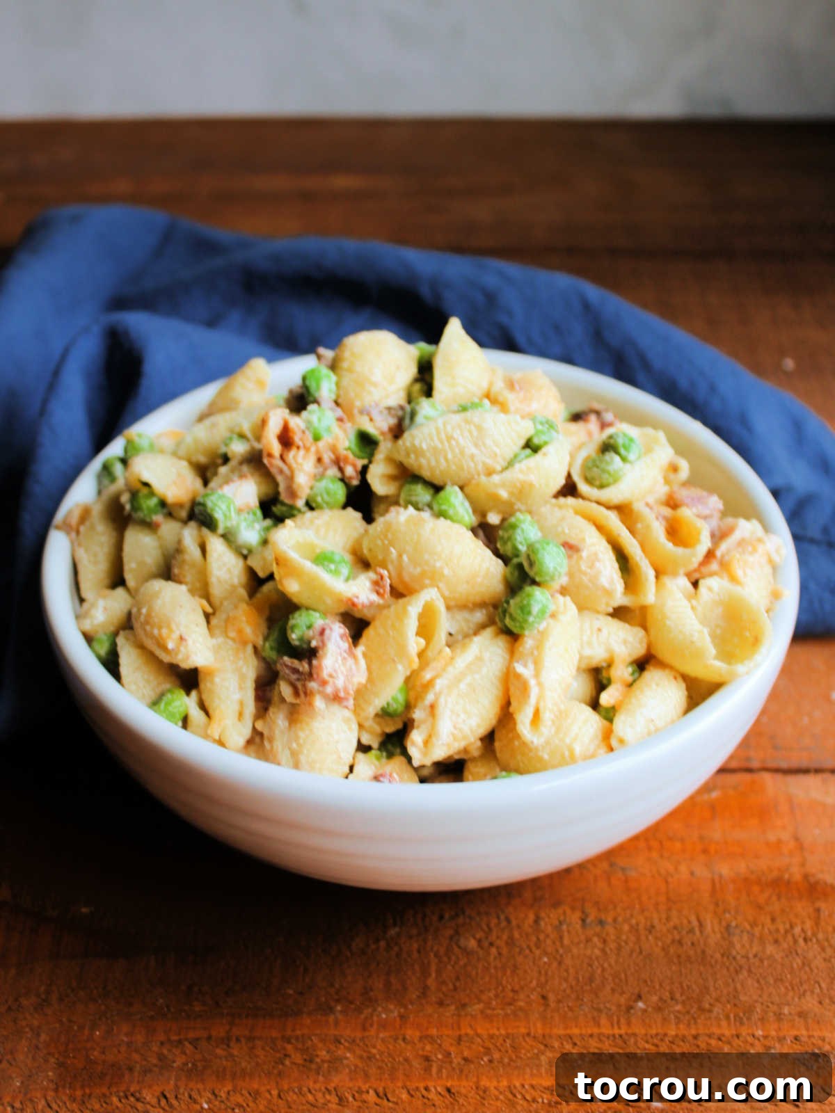Bowl of creamy macaroni salad with peas, bacon, and cheese after it has been chilled and transferred to an elegant serving bowl, ready for presentation.
