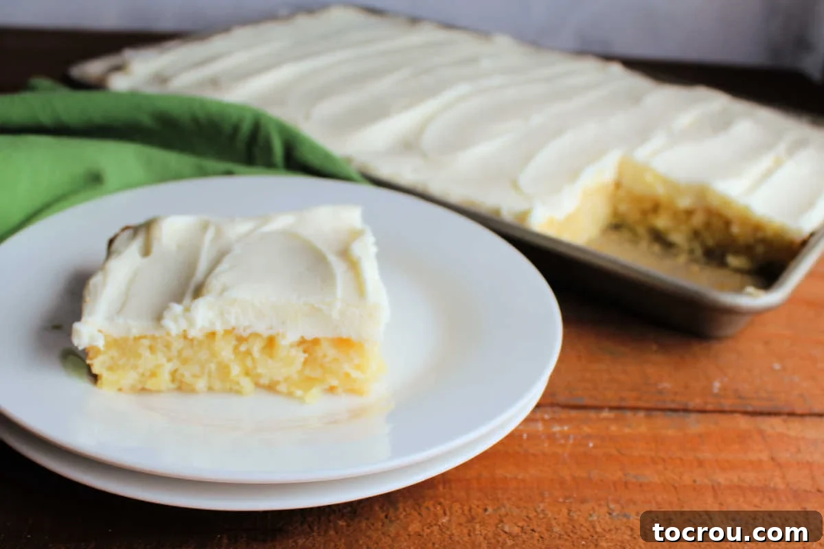 Pineapple Sheet Cake Slice A delectable slice of pineapple sheet cake on a dessert plate, showcasing its moist texture and generous layer of cream cheese frosting. The rest of the cake is visible in the background, ready to be enjoyed.