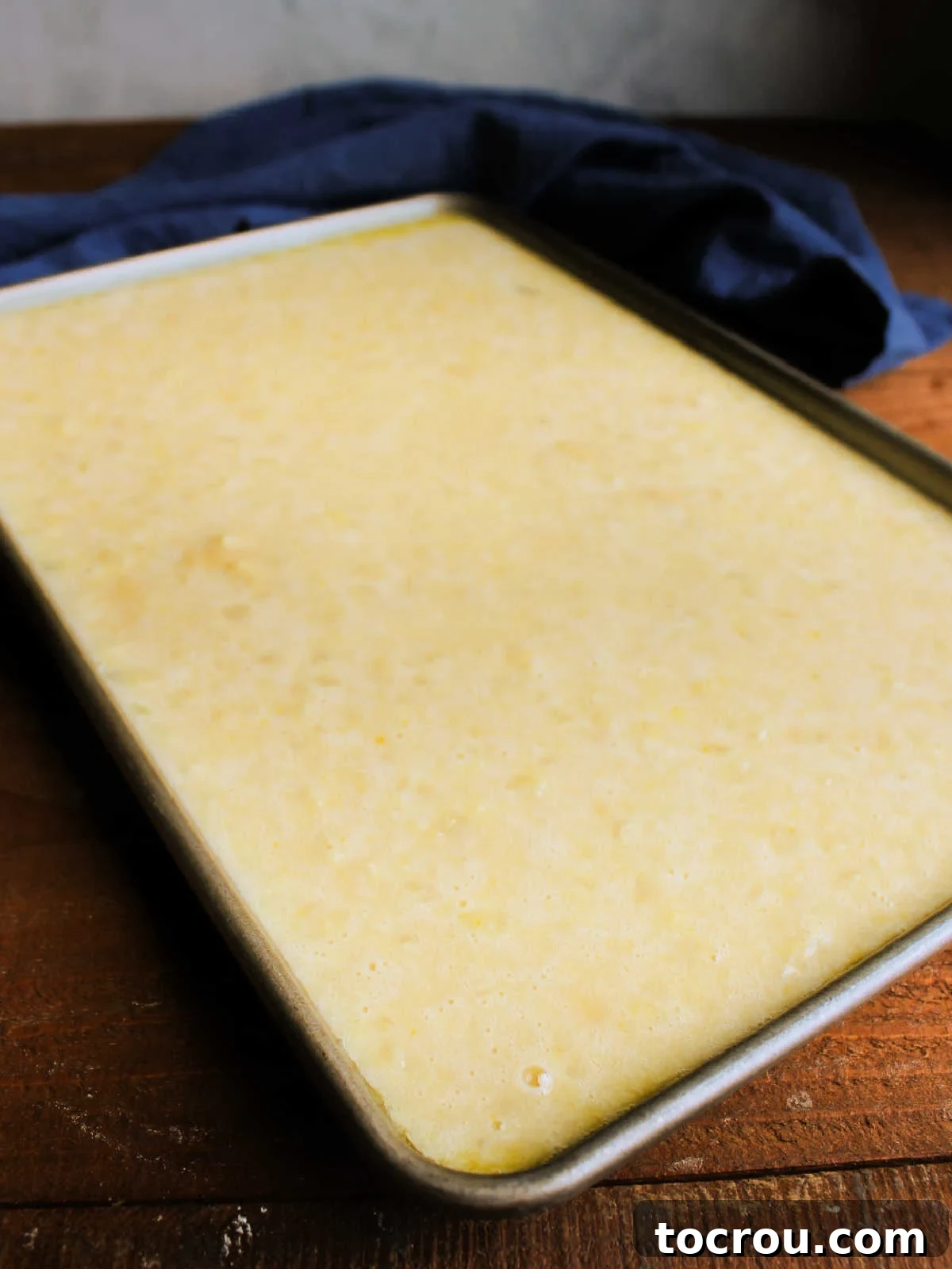 Pineapple Cake Batter in Pan Smooth, golden pineapple cake batter spread evenly in a 10x15-inch sheet cake pan, ready for baking.