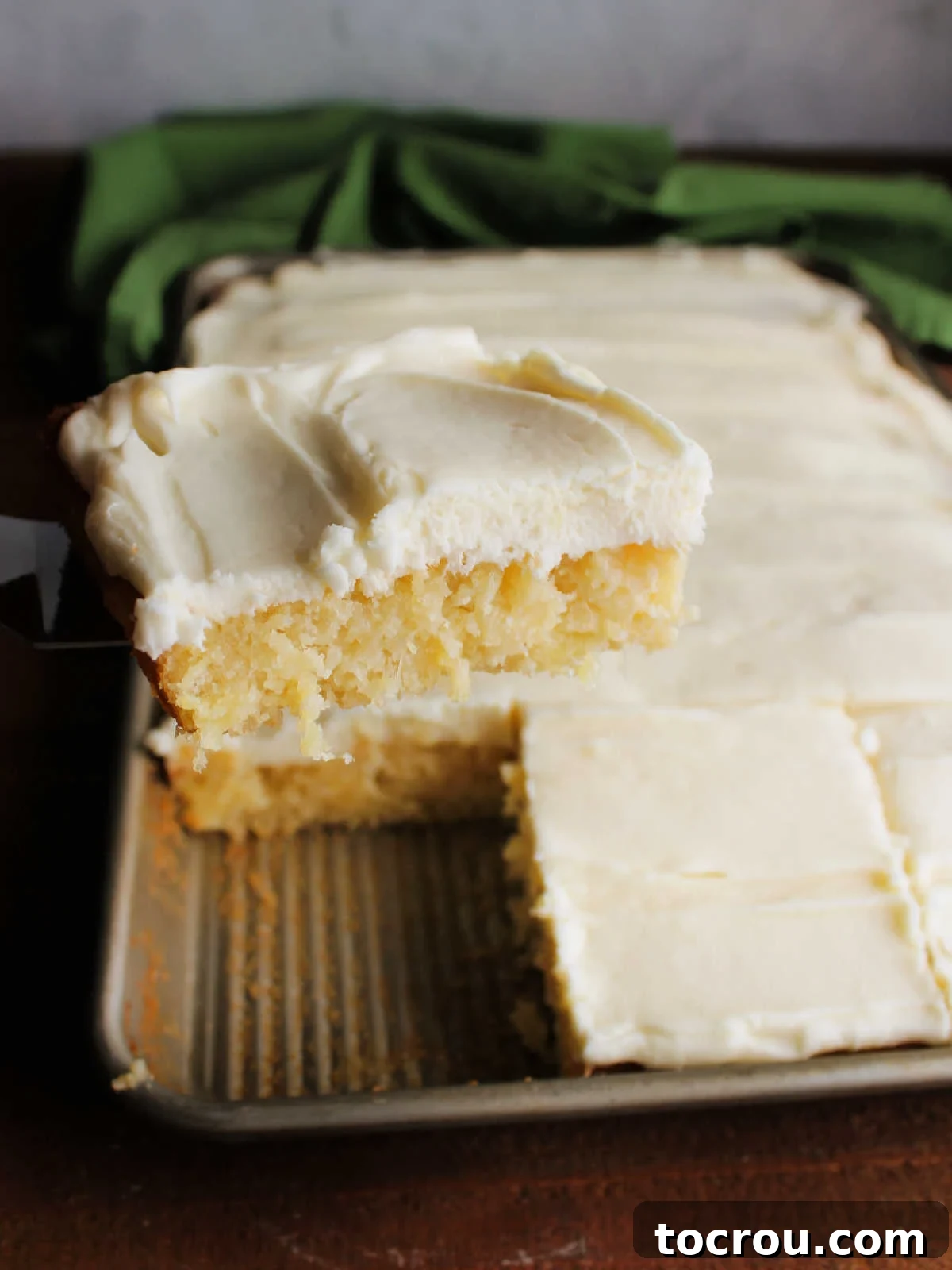 Serving Pineapple Sheet Cake A spatula gently lifting a perfect slice of pineapple sheet cake, revealing its fluffy texture and the rich cream cheese frosting, from the baking pan.