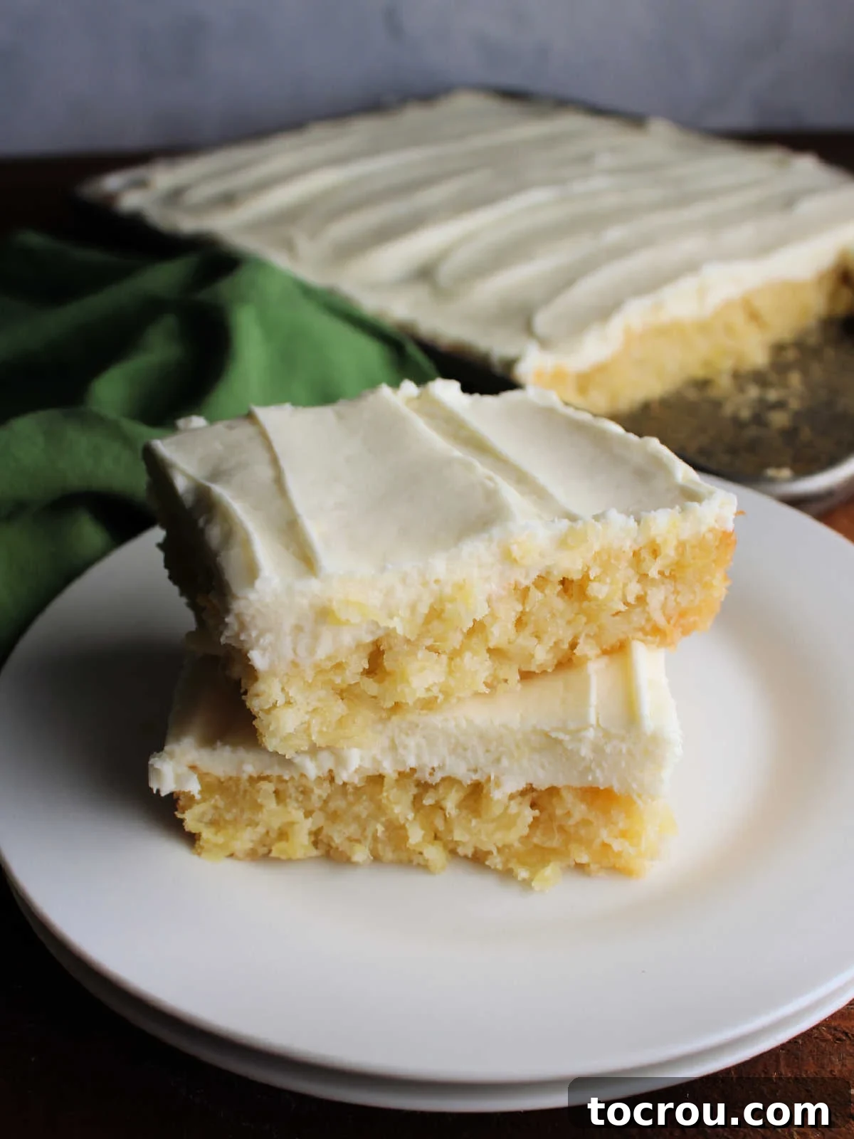 Ready-to-Eat Pineapple Cake Slices Multiple slices of pineapple sheet cake, elegantly frosted with cream cheese, arranged on a plate, inviting you to take a bite.