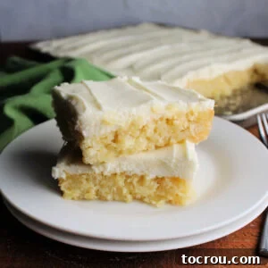 Two generous pieces of pineapple sheet cake, elegantly frosted with cream cheese, stacked on top of each other, ready to be enjoyed.