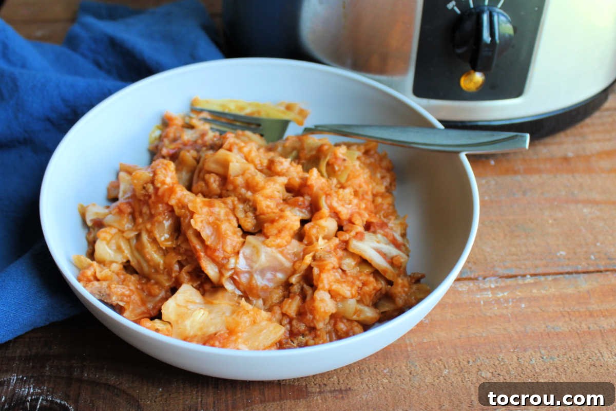 Bowl of crockpot cabbage roll casserole with cabbage, rice, and sausage in tomato sauce, ready to eat.