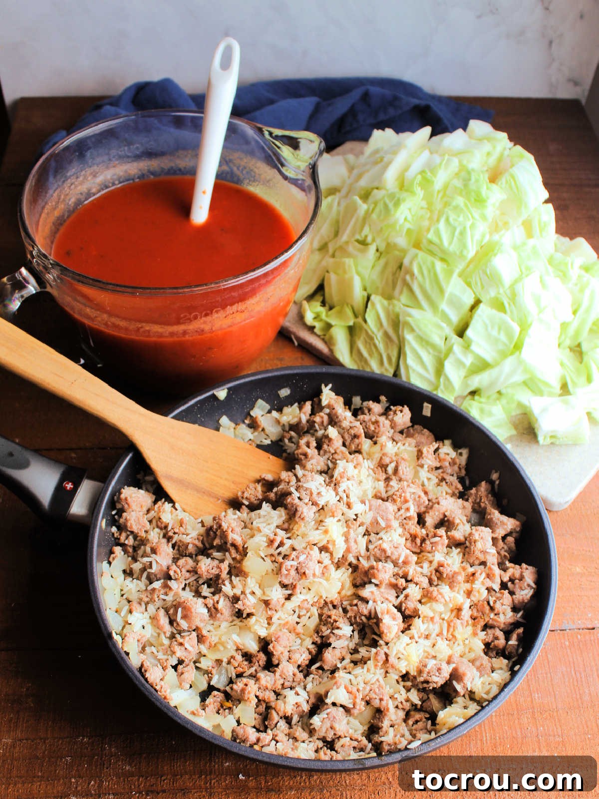 Ingredients including cooked sausage, onion, rice, cabbage and a tomato sauce ready to be put in crockpot to make cabbage roll casserole.