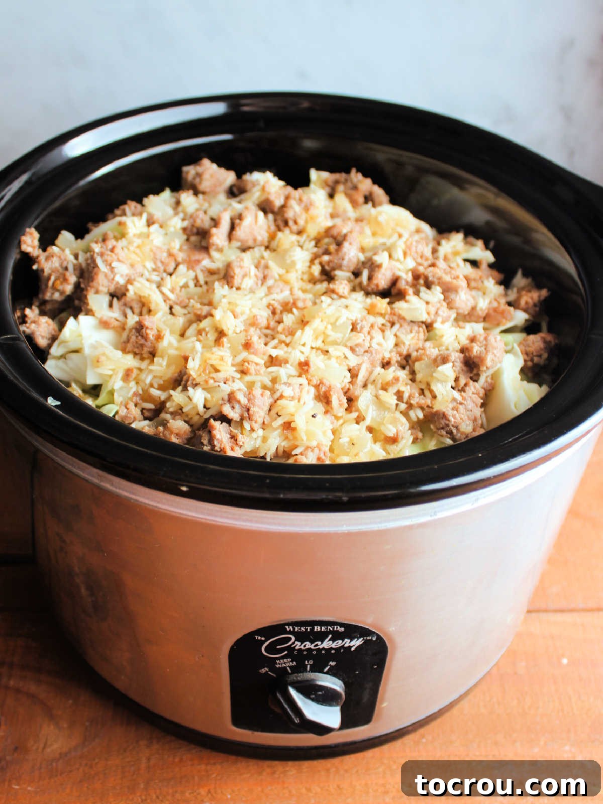 Layers of chopped cabbage, meat, and rice layered in slow cooker.