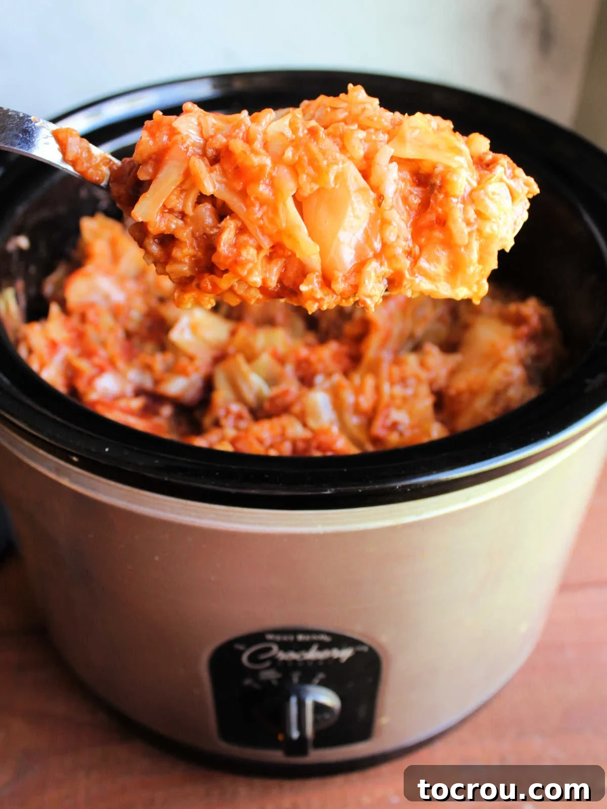 Serving spoon scooping out cabbage roll casserole with tomato sauce, cabbage, rice, and sausage.