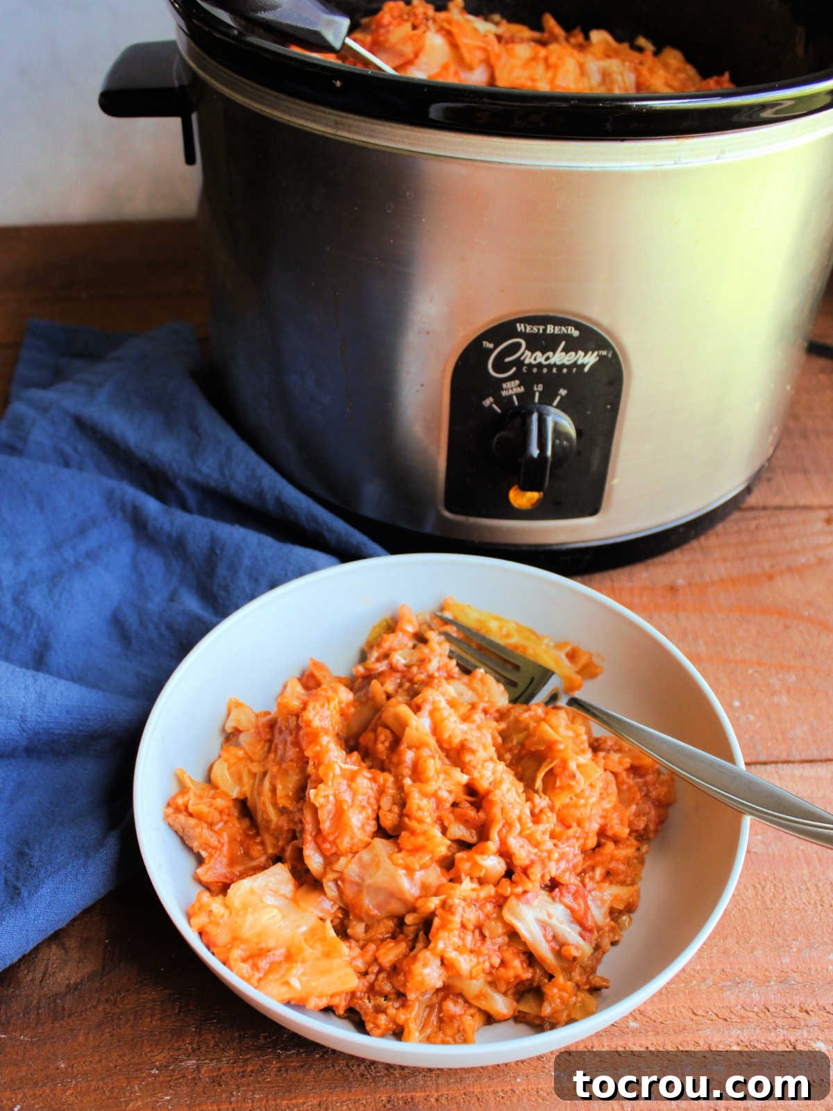Bowl of slow cooker stuffed cabbage casserole with crockpot and remaining mixture in the background.