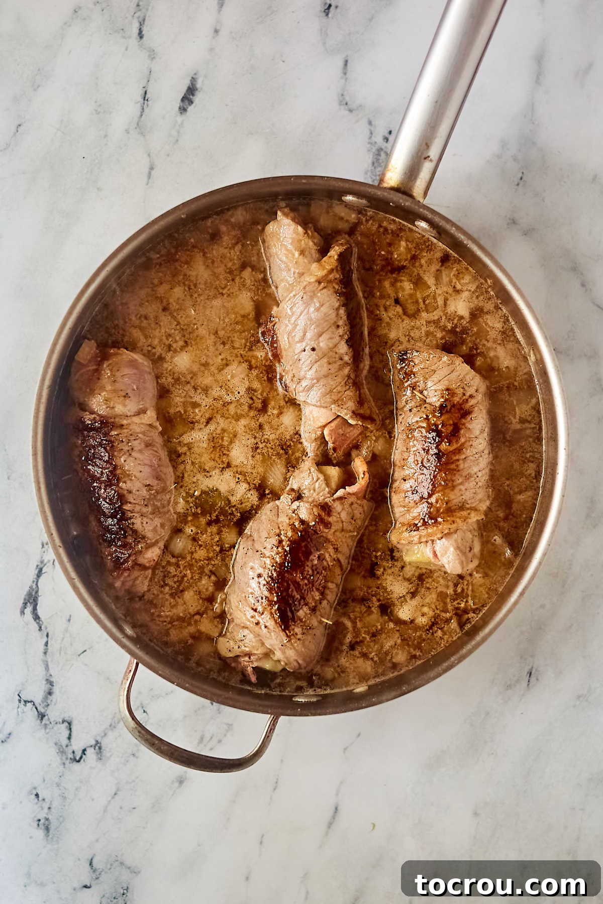 Rouladen after they have simmered in the beef broth and onion mixture.