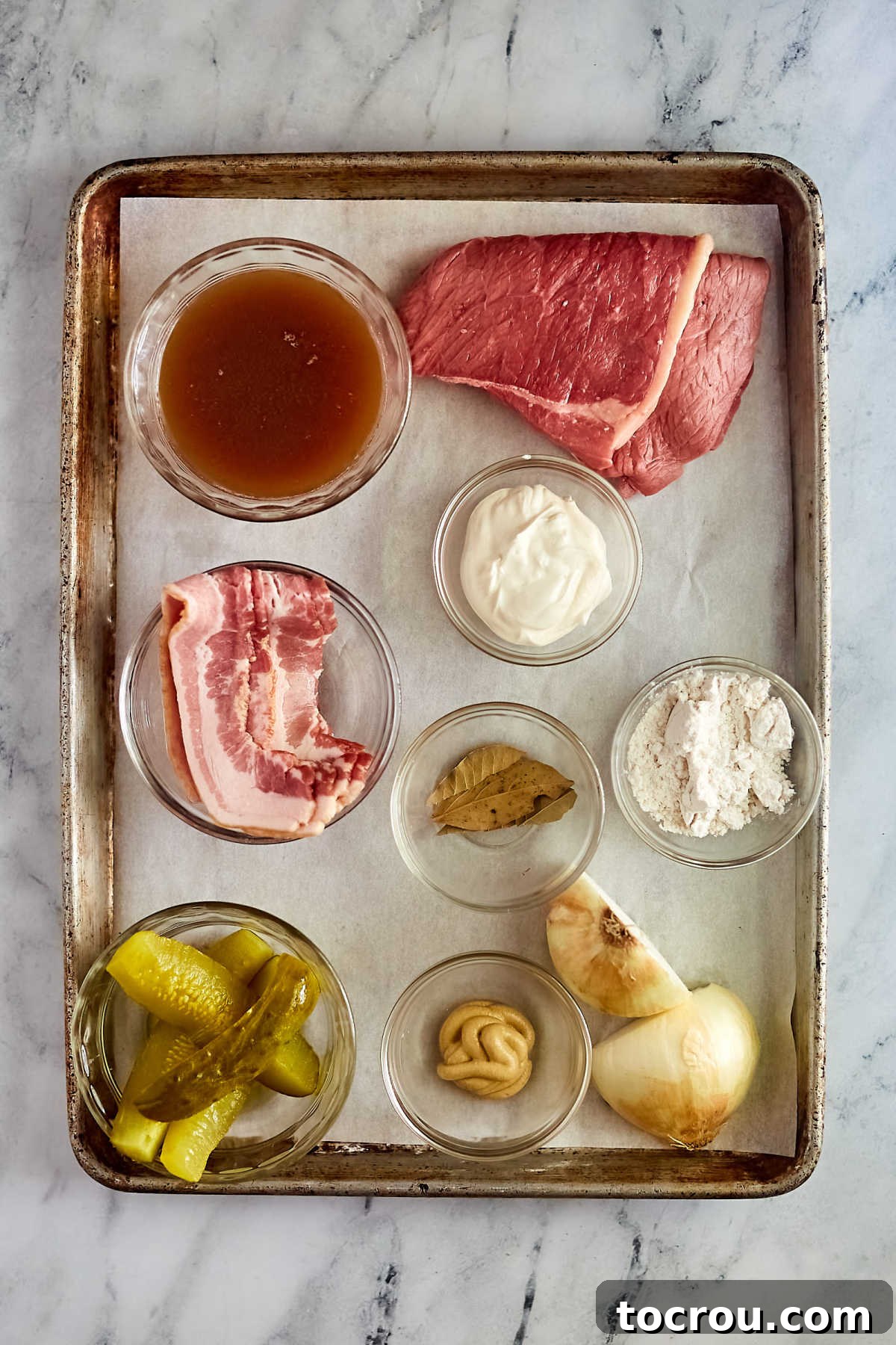 Ingredients including thin beef steaks, bacon, onions, pickles, mustard, beef broth, flour, and sour cream, ready to be made into beef rouladen. 
