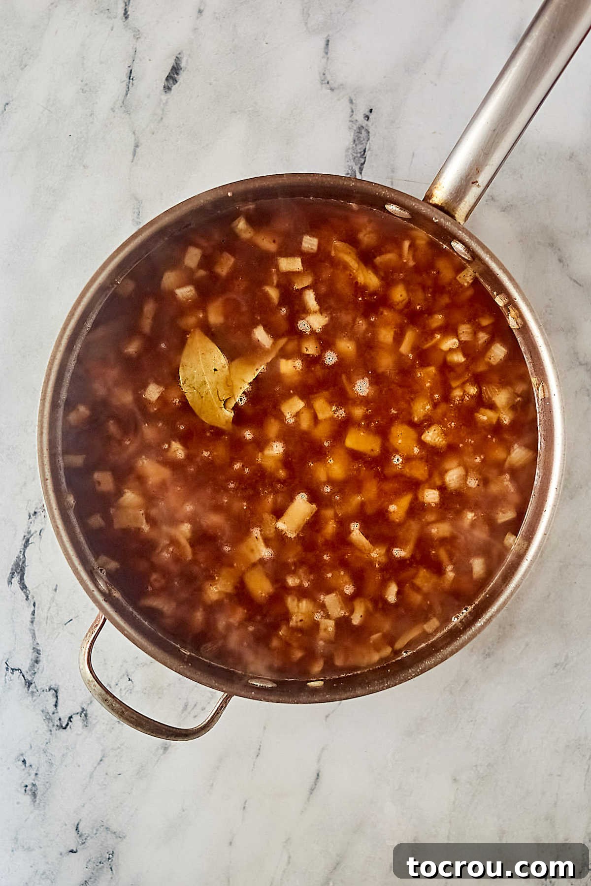 Pan filled with sauteed onions, beef broth, and bay leaf. 