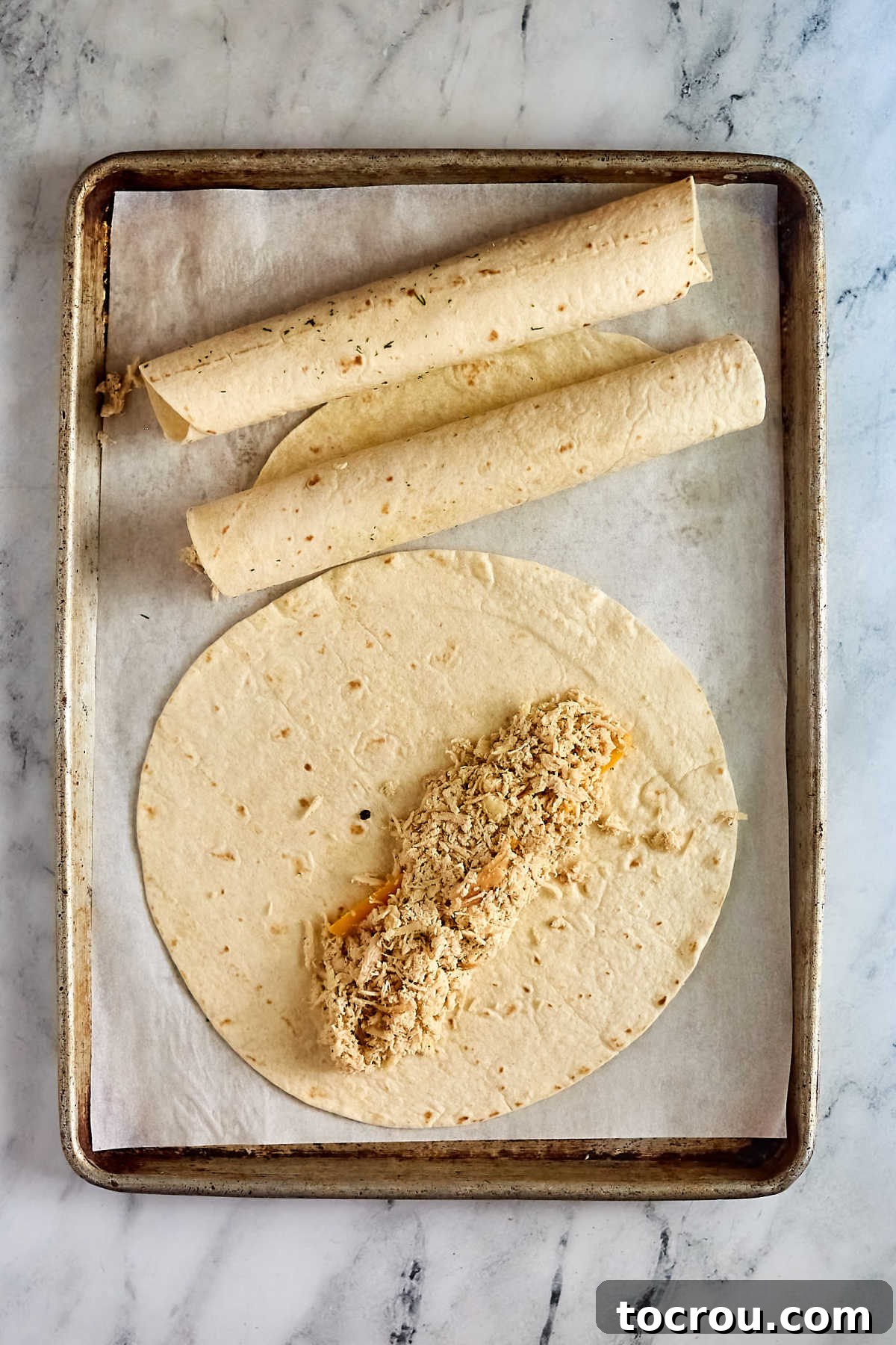 Rolling Enchiladas Someone wrapping a mixture of shredded chicken and cheese in flour tortillas to form enchiladas for baking.