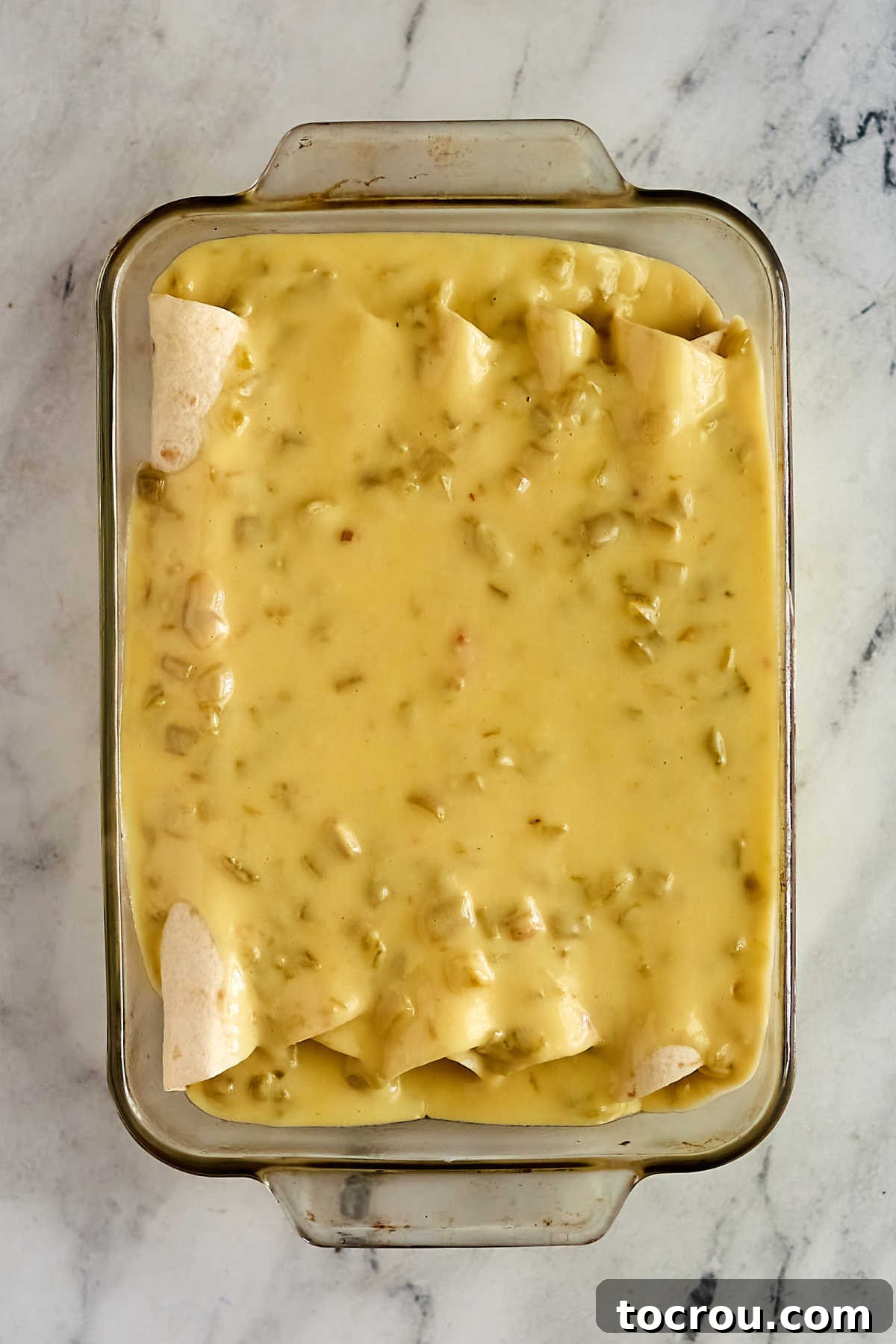 Enchiladas Ready for Oven A baking dish filled with assembled chicken enchiladas, generously covered in creamy white sauce, ready to be placed in the oven.