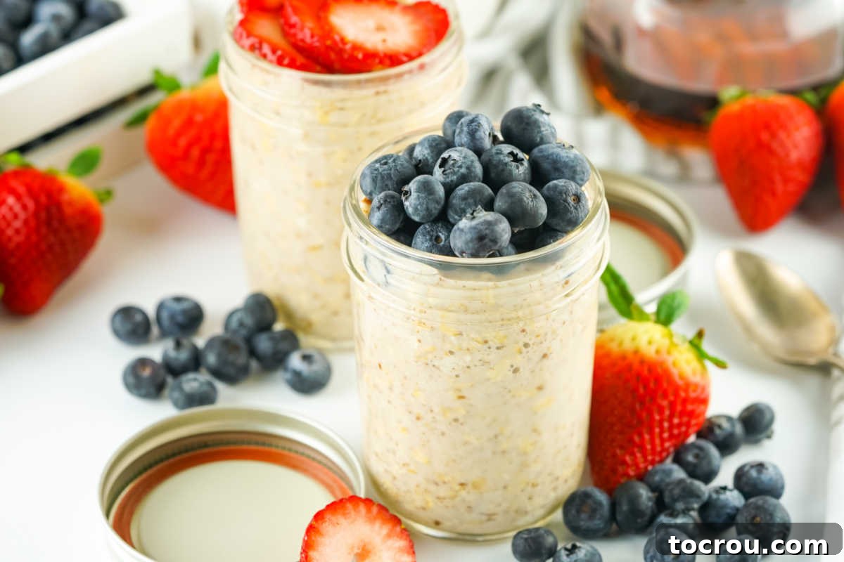 Velvety Overnight Oats 2 Two jars of creamy overnight oats, one topped with fresh strawberry slices and the other with fresh blueberries.