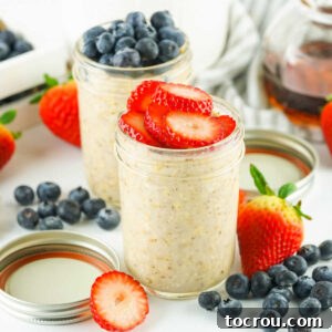 Velvety Overnight Oats 8 Two jars of creamy overnight oats, one topped with fresh strawberry slices and the other with fresh blueberries.
