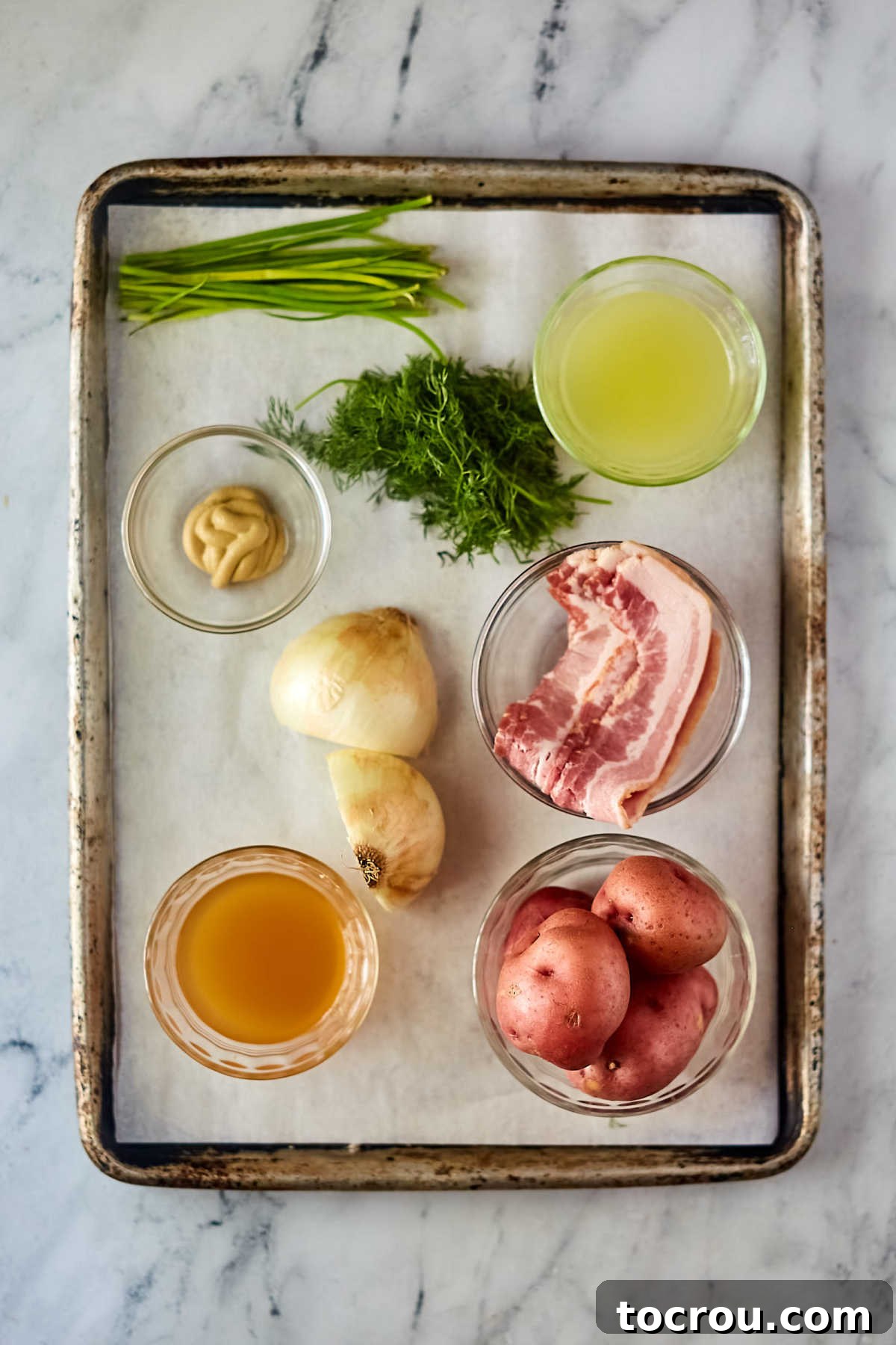Ingredients including red potatoes, bacon, onion, mustard, vinegar, and herbs ready to be made into German potato salad. 