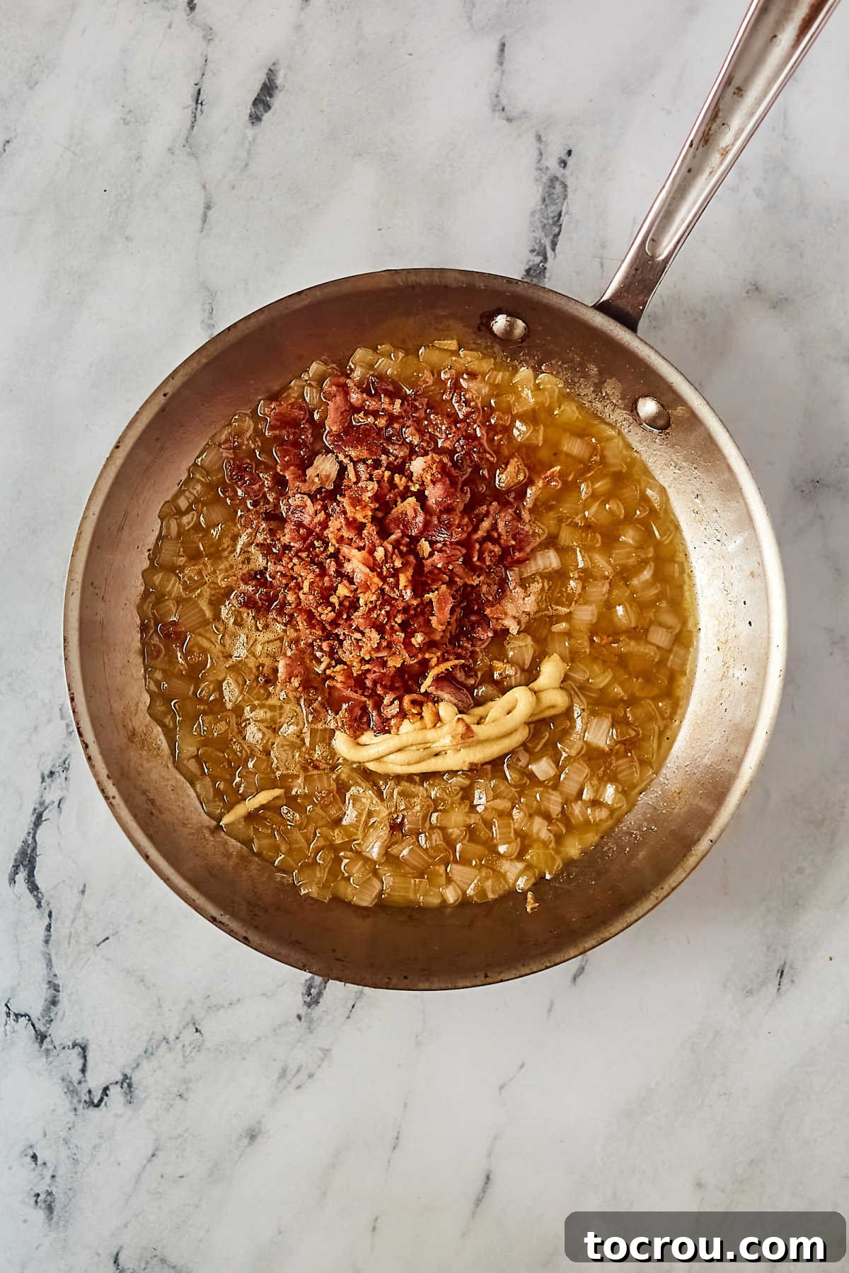 Making German potato salad dressing in skillet with cooked onions, mustard, chopped bacon and vinegar. 