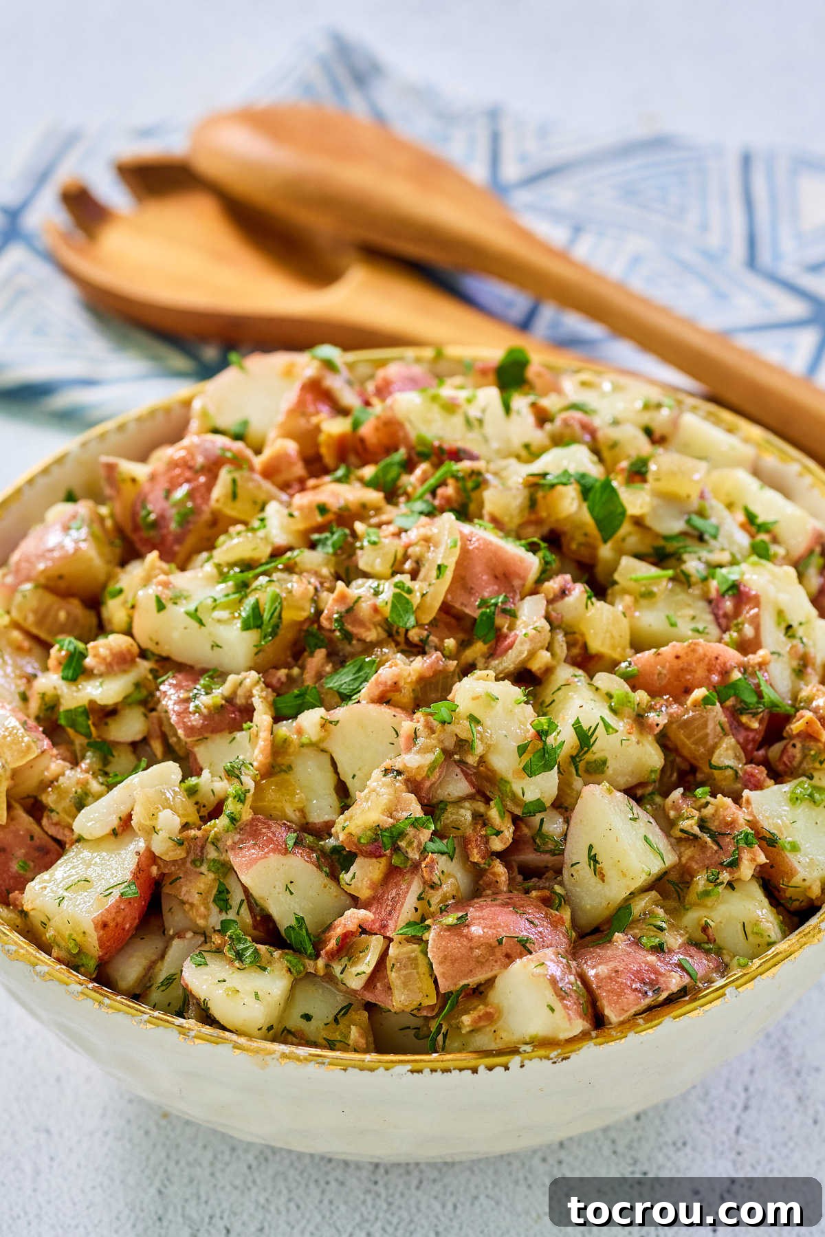 Close up of German potato salad showing chunks of bacon and potatoes in light dressing topped with fresh herbs. 