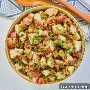 Bowl of german potato salad with cubed red potatoes, bacon, a light dressing and fresh herbs, ready to serve.