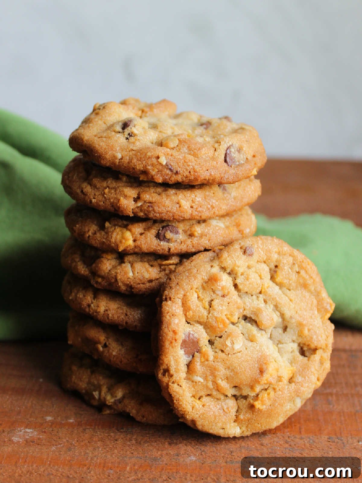 Tall stack of cornflake cookies with chocolate chips with one leaning against the tower, showing texture.