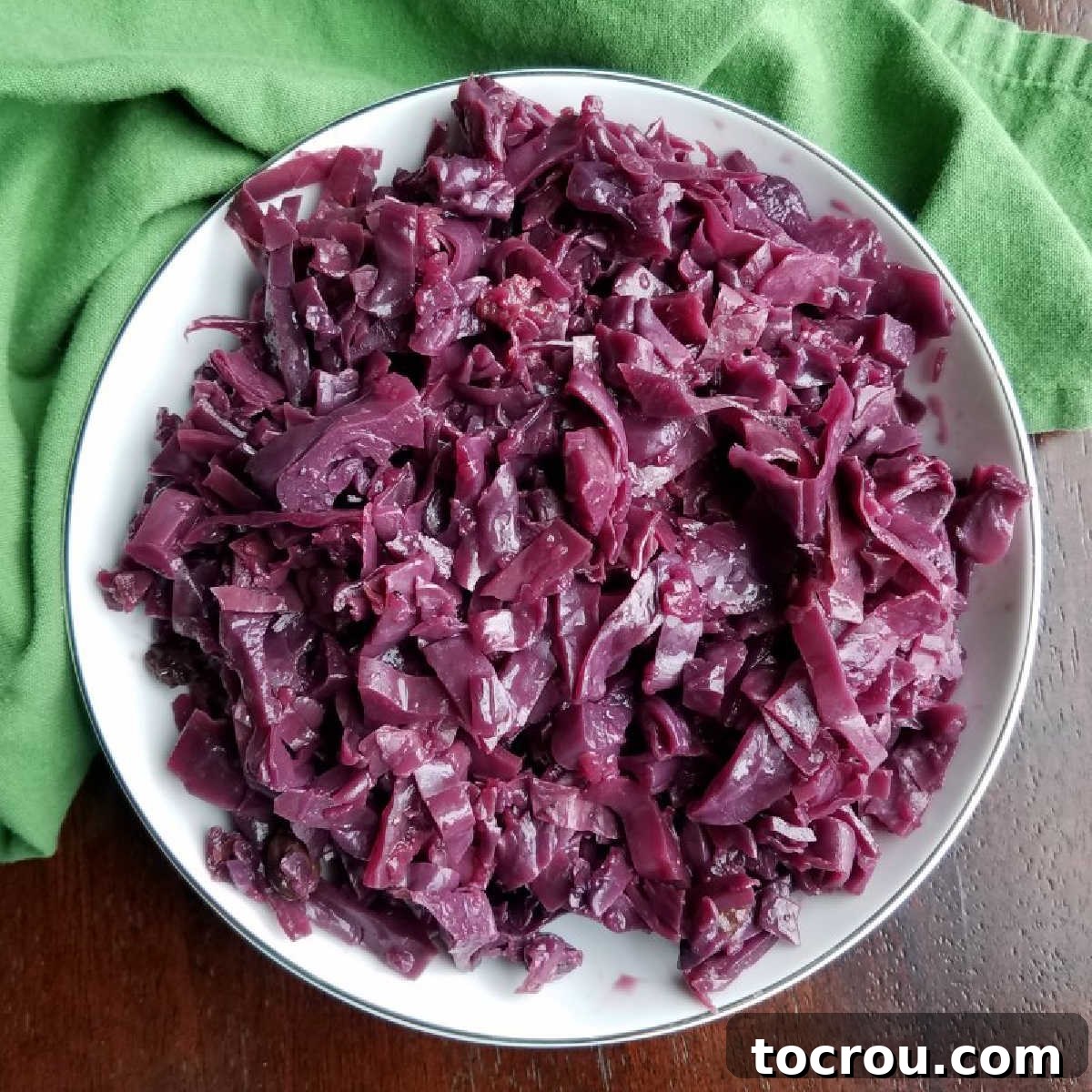 German-style braised red cabbage with apples and spices, a perfect sweet and sour side for pork. A beautiful bowlful of vibrant braised red cabbage, garnished with glossy apples and plump raisins, ready to be served.