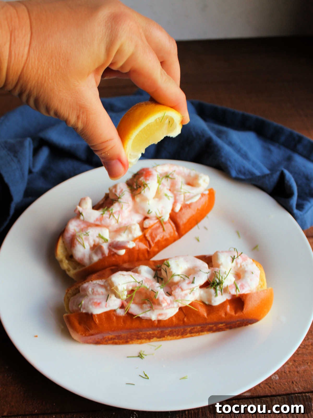 Hand squeezing lemon wedge over a shrimp roll with mayonnaise dressing. 