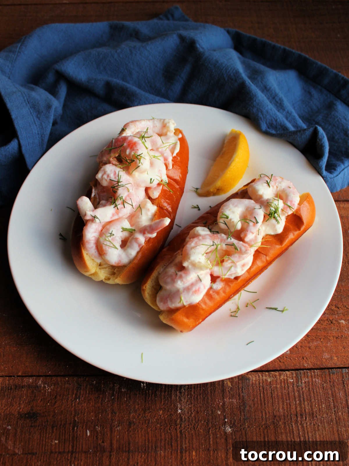 Plate with two shrimp rolls with brown butter and may coated shrimp in toasted brioche buns. 