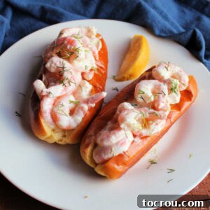 Two shrimp rolls with buttery toasted brioche buns piled high with shrimp in mayo and brown butter mixture with lemon wedge and fresh dill, ready to eat.