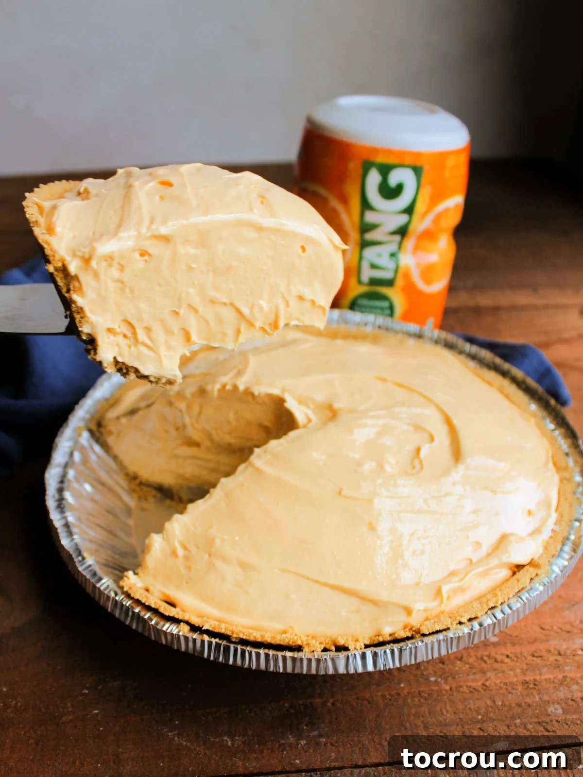 Golden Tang Delicacy 7 Pie serving lifting a slice of chilled Tang pie out of the tin, showing creamy texture.