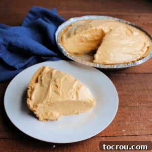 Slice of creamy no-bake tang pie on plate with remaining pie in graham cracker crust in the background.