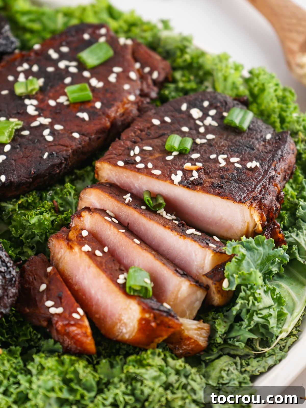 Slices of marinated pork chops garnished with sesame seeds and scallions on a bed of greens. 