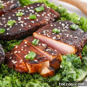 Pork chop sliced into thick slices with dark brown soy sauce soaked exterior and light pink interior garnished with sesame seeds and green onions.