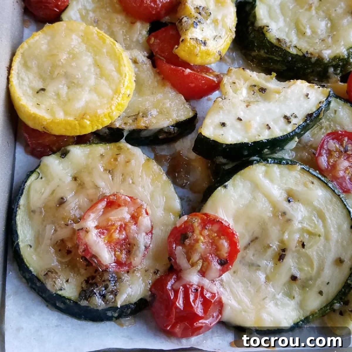 Close-up of golden brown Parmesan roasted zucchini and cherry tomatoes, fresh from the oven, with melted cheese and seasonings on the perfectly cooked vegetables.