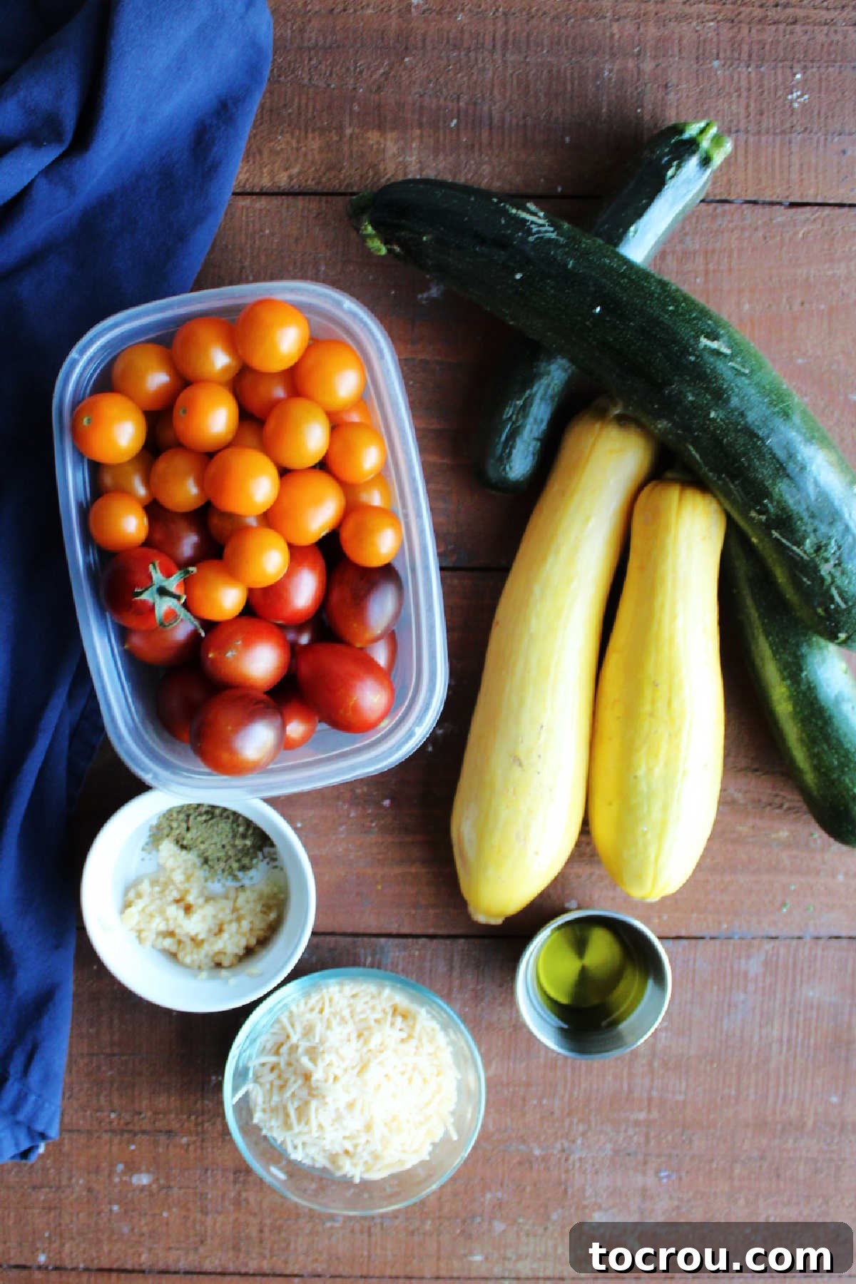Ingredients for baked zucchini and tomatoes with cheese including sliced zucchini, yellow squash, halved cherry and grape tomatoes, grated parmesan cheese, olive oil, and various seasonings, ready for preparation.