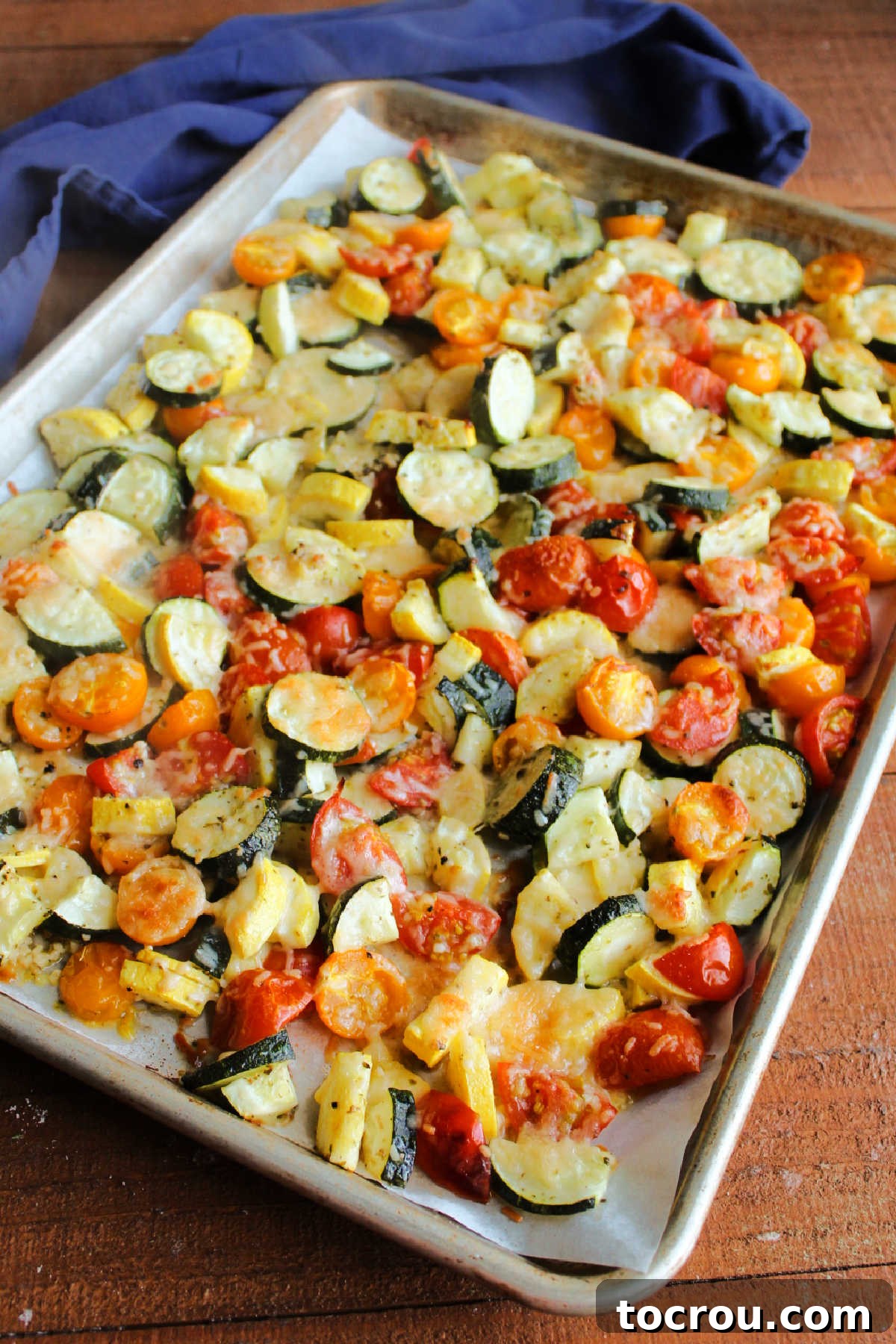 Sheet pan brimming with perfectly baked zucchini and tomatoes, generously topped with melted, golden-brown Parmesan cheese, ready to be served hot.