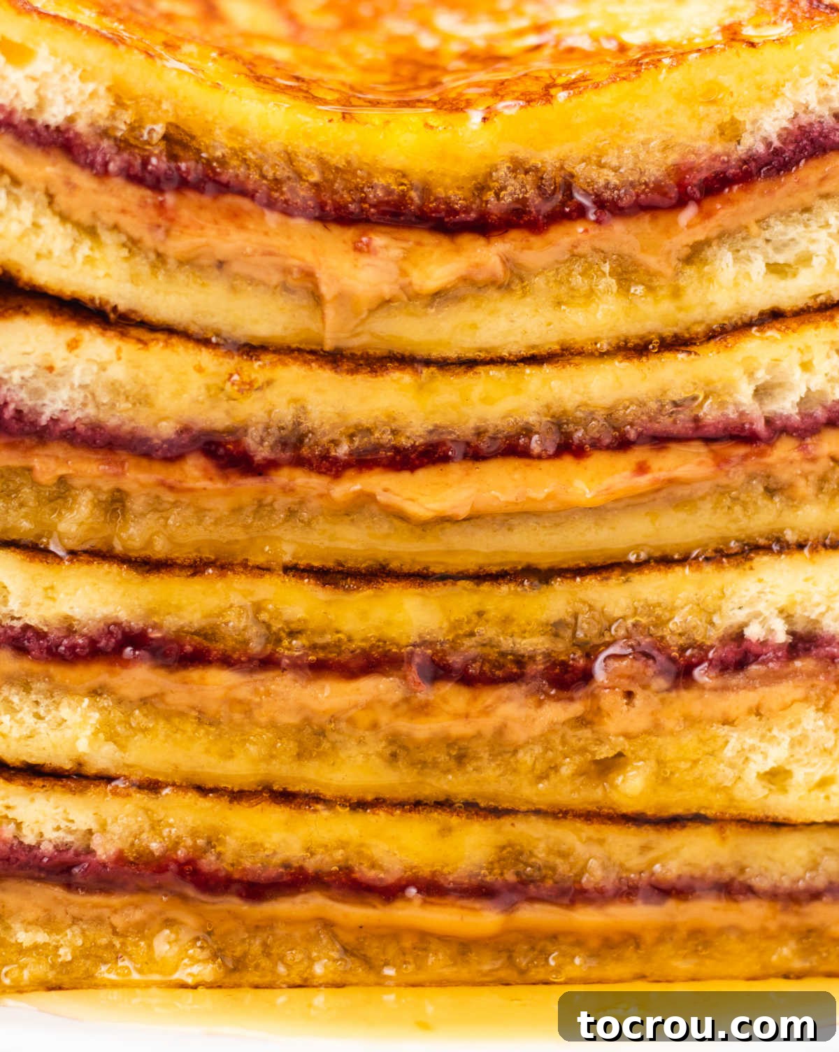 Peanut Butter and Jelly Stuffed French Toast 7 Close up of a stack of peanut butter and jelly french toast halves showing warm and gooey peanut butter and jam between cooked custard soaked bread with crisp edges.