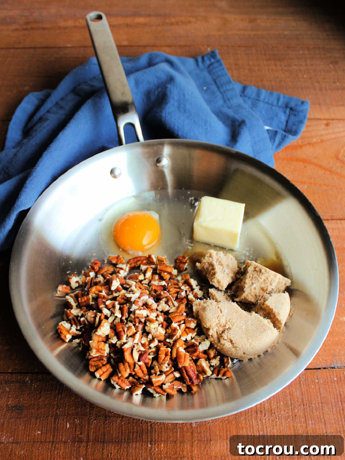 Ingredients including brown sugar, corn syrup, egg, pecan pieces, salt, and butter in skillet ready to be made into pecan pie dip topping.