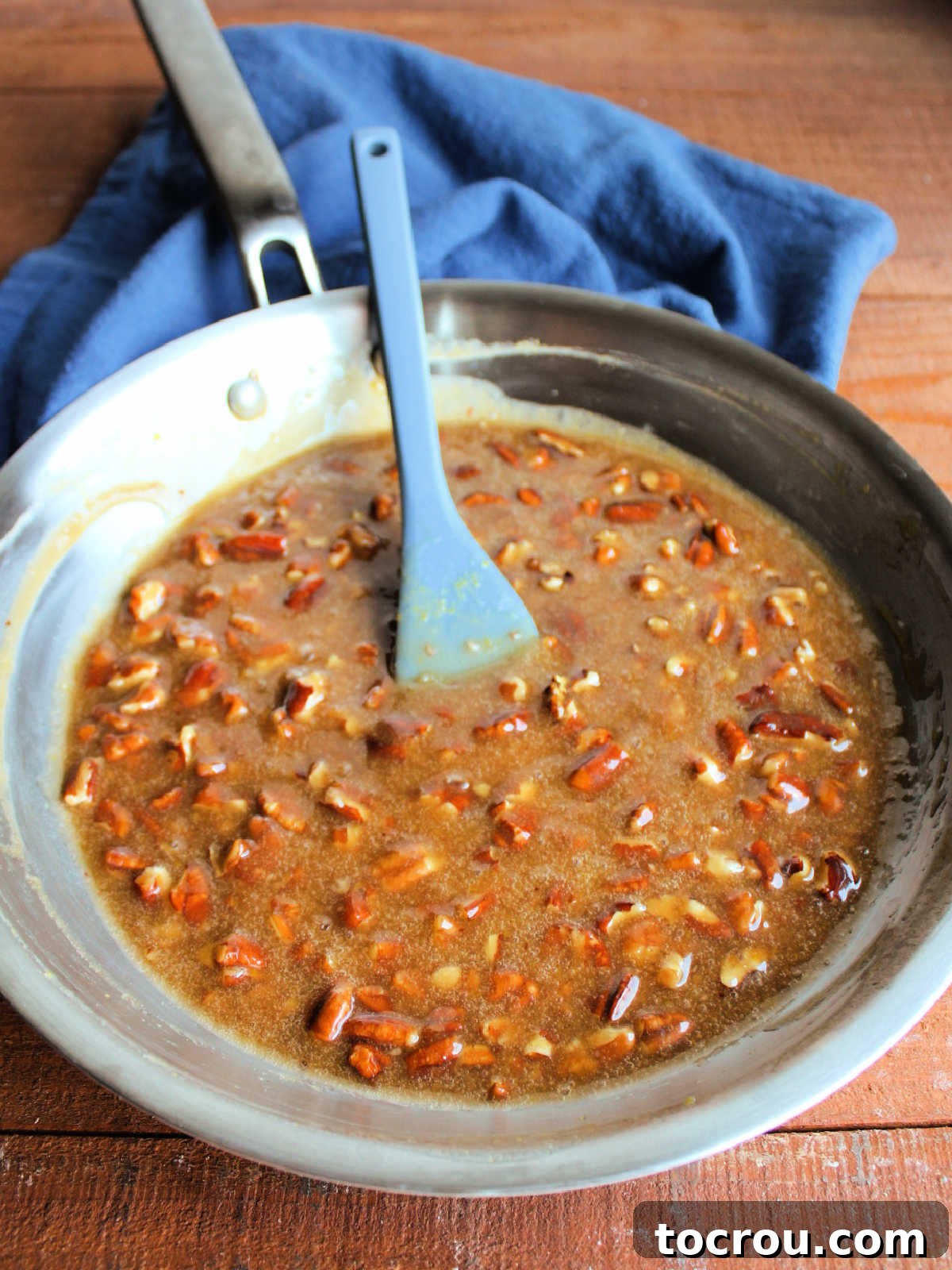 Skillet filled with gooey pecan pie mixture after it has been cooked, ready to go on the cream cheese layer.