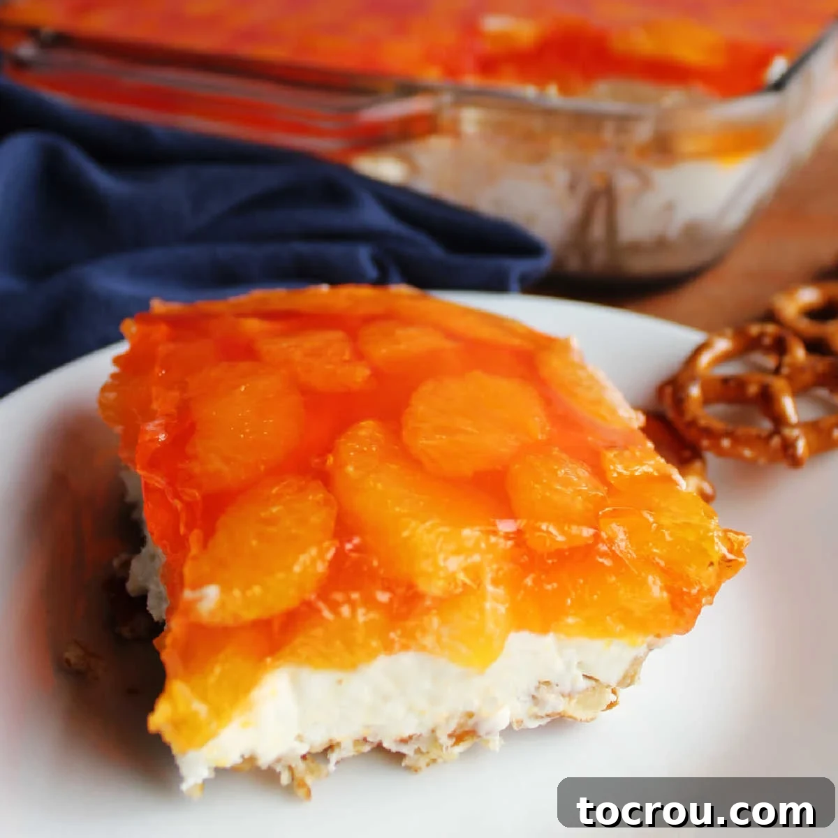 Close-up piece of orange pretzel salad showing crumb crust, creamy vanilla center, and topping made from orange jello and mandarin oranges.