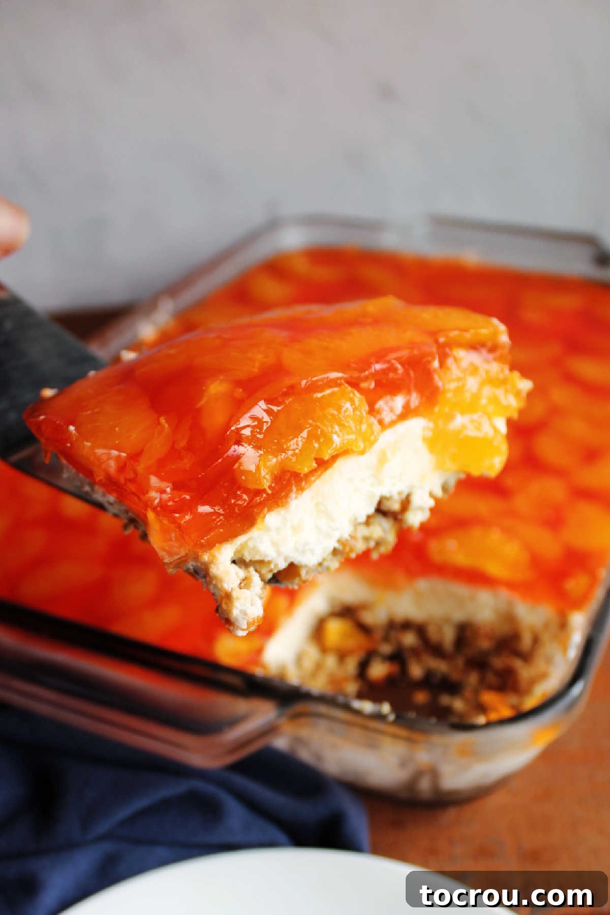 Spatula lifting piece of mandarin orange jello salad out of pan, showing layers.