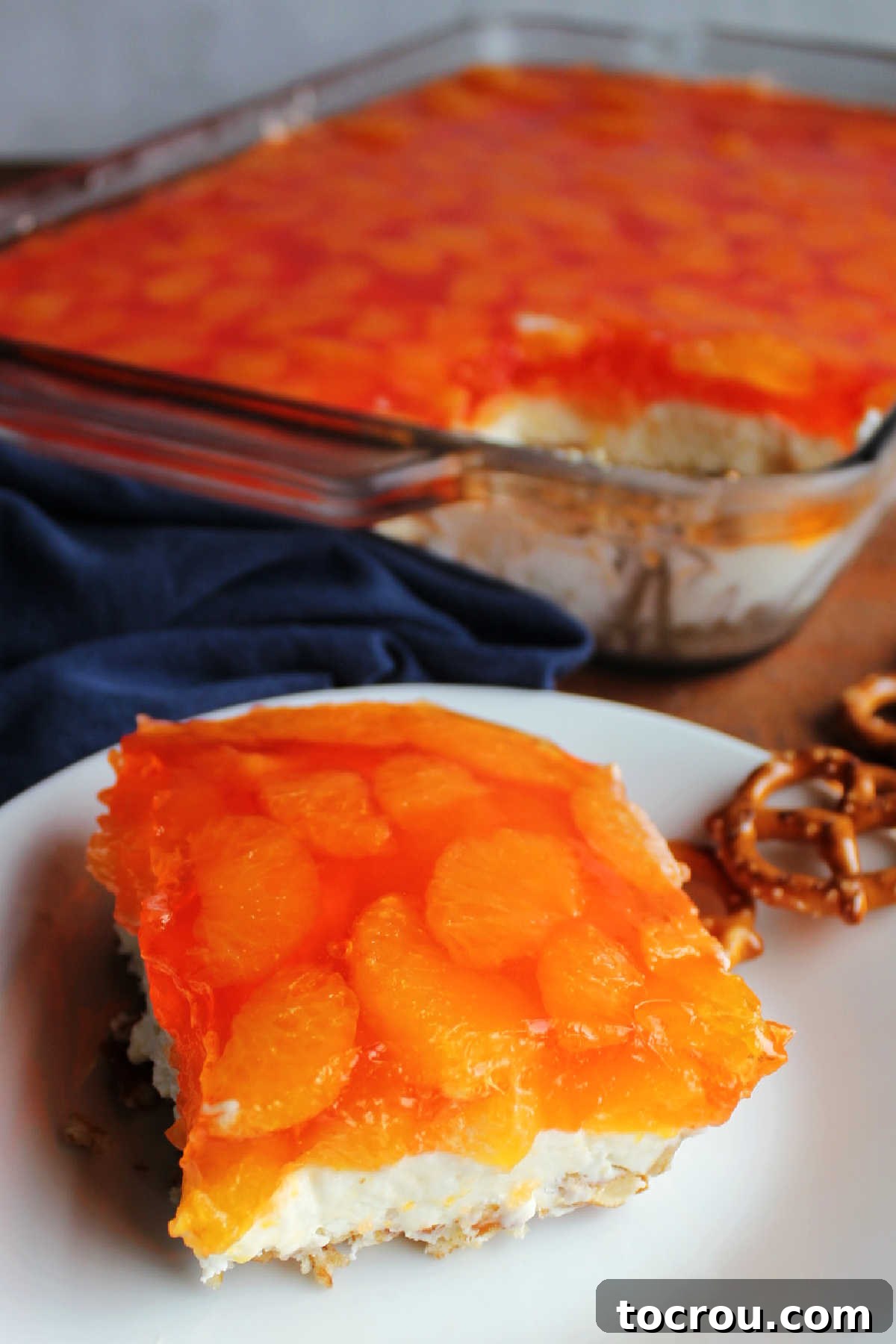 Piece of mandarin orange pretzel salad served on small plate with remaining pan in the background.